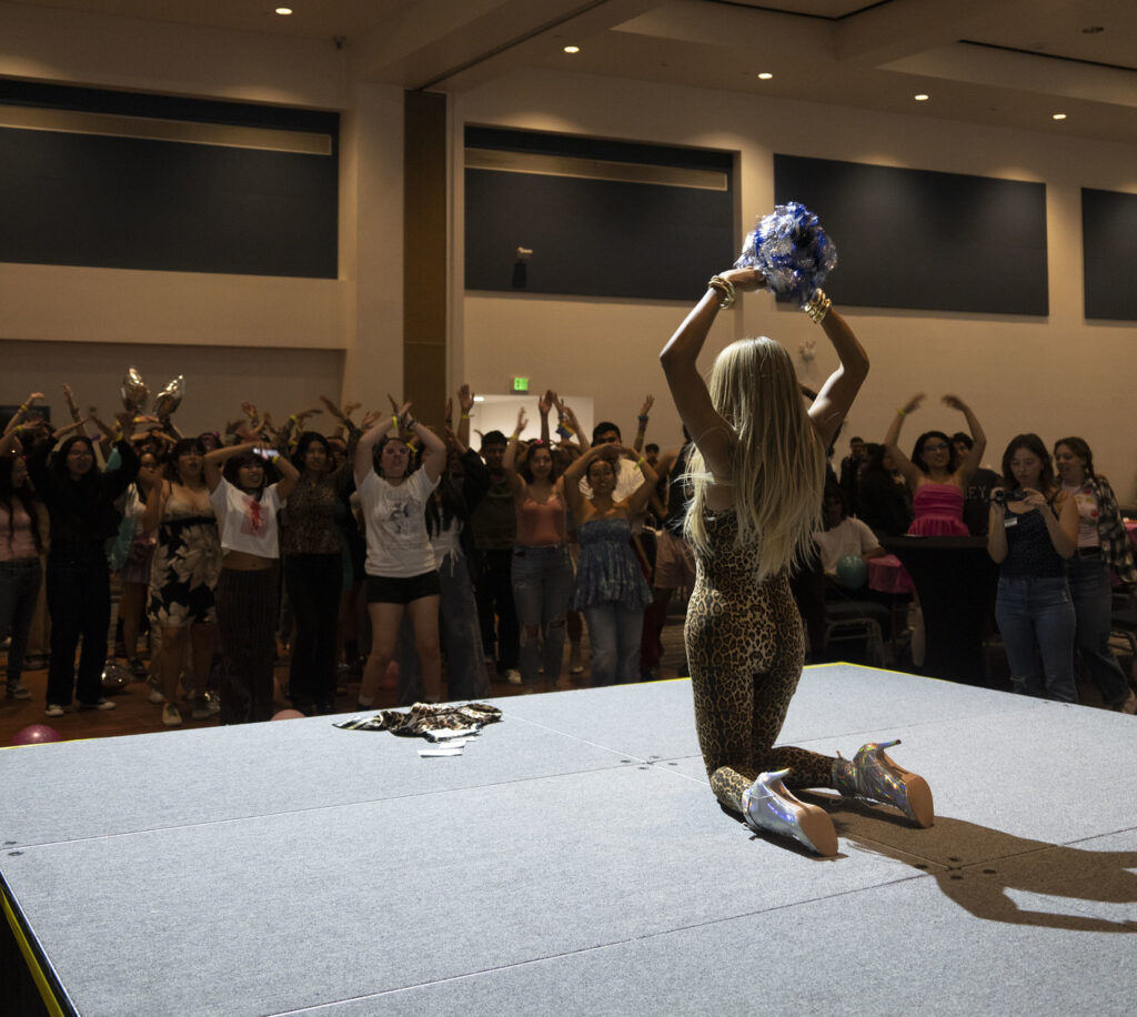 Crowd of 30+ people following along with a drag queen holding pompoms.