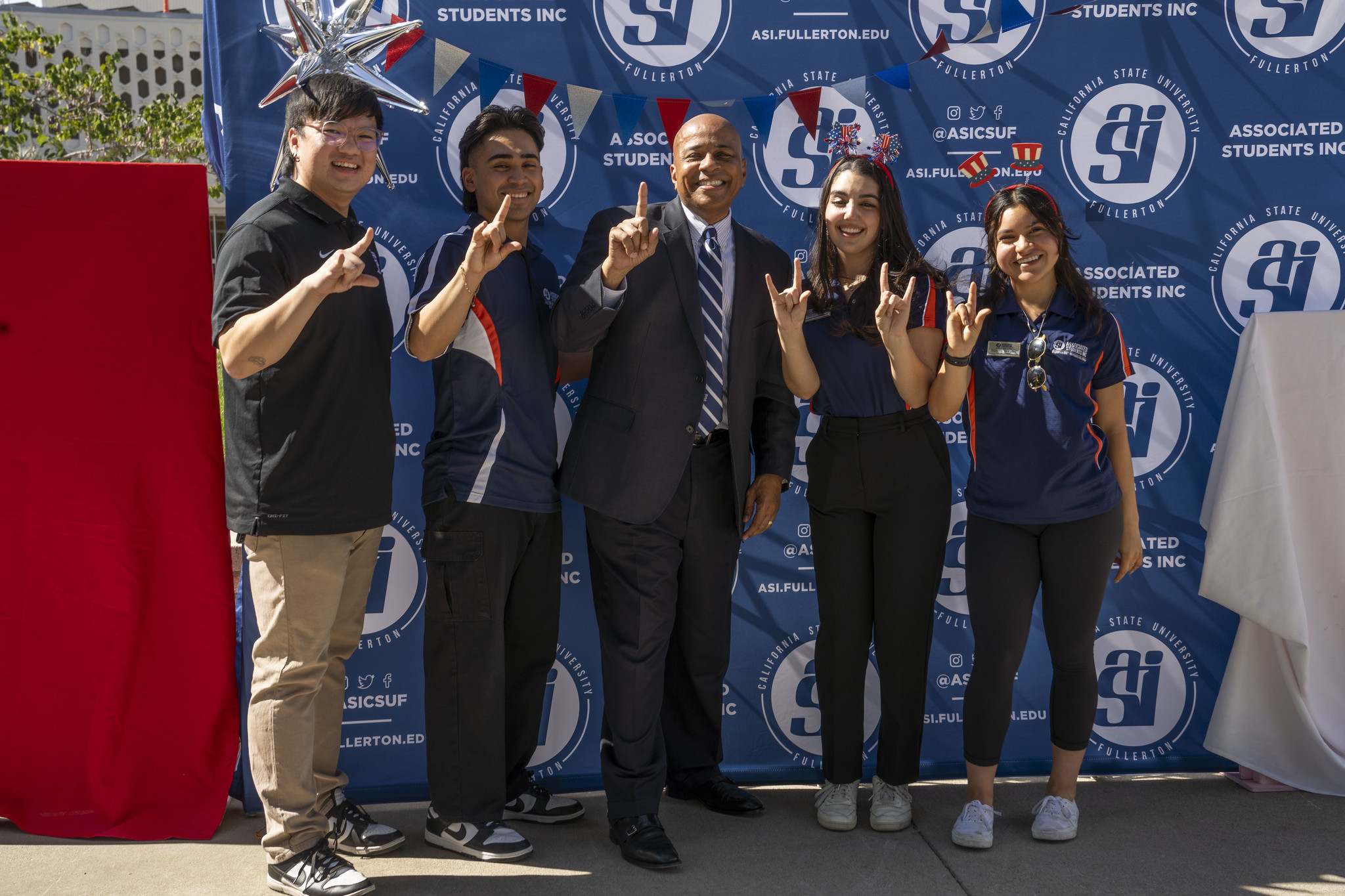 Four student government officials and president Rochon pose in front of the ASI banner