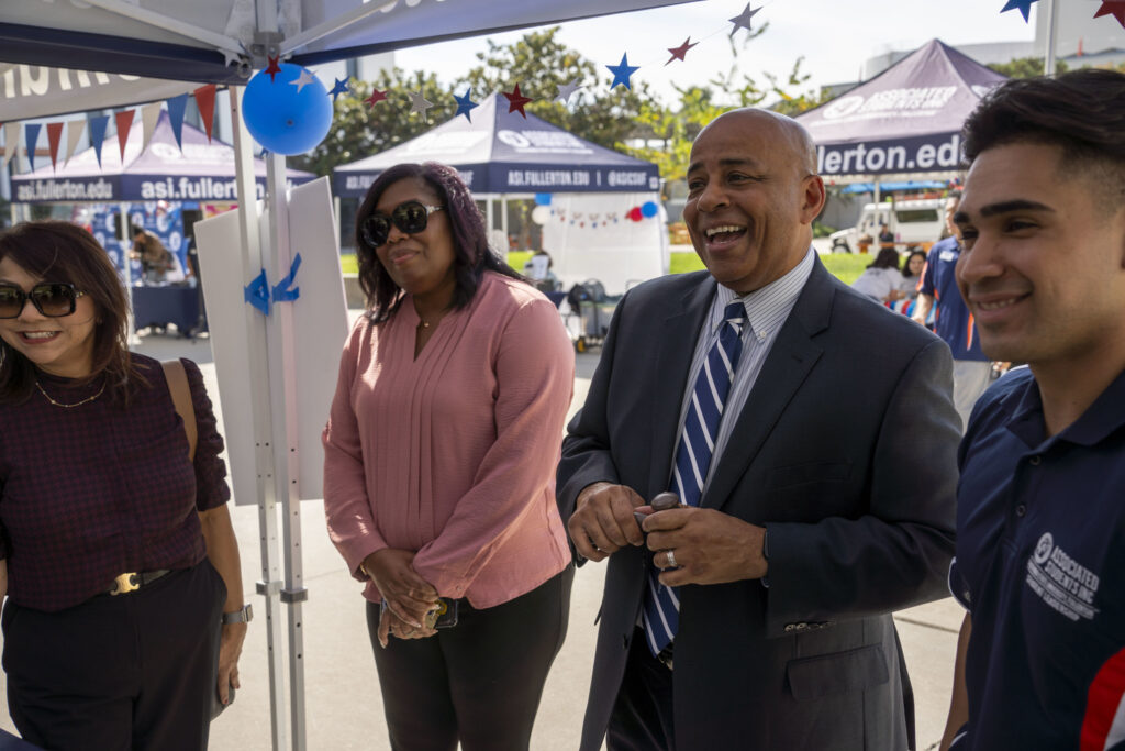 Two men and Two women stand smiling as they listen to something.