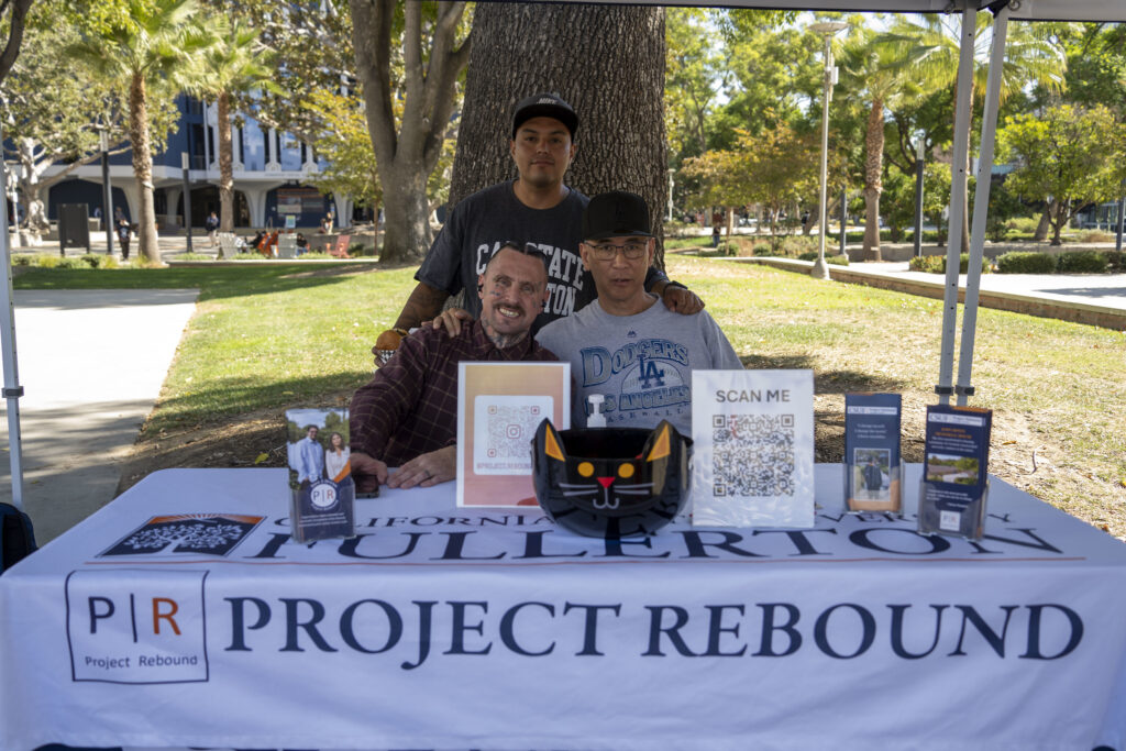 Three men sit behind a table with different resources for students.