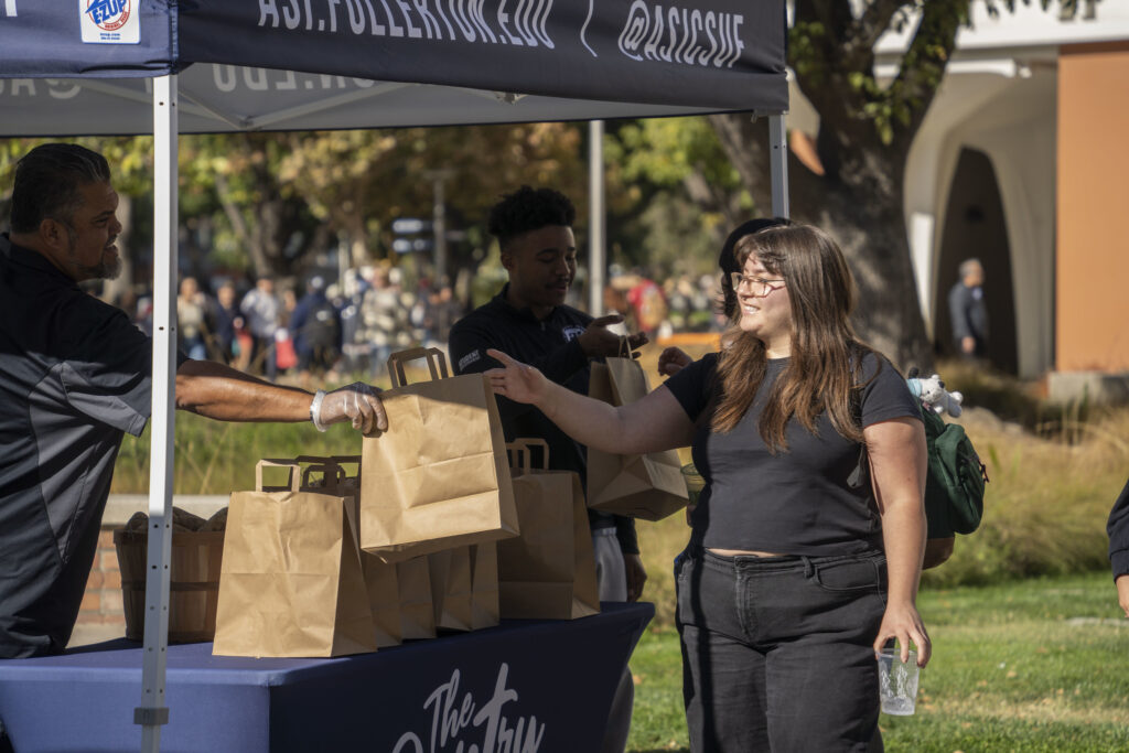 A man smiles as her hands a brown paper bag to a smiling event participant.