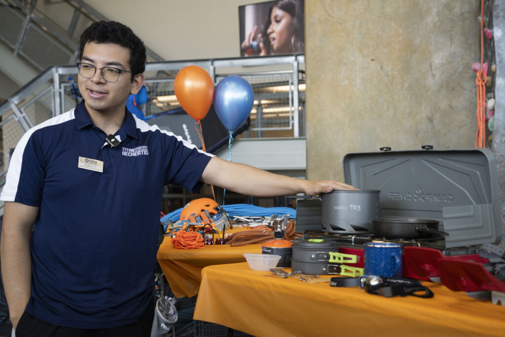 A titan outdoors member gestures to outdoor equipment on a table.