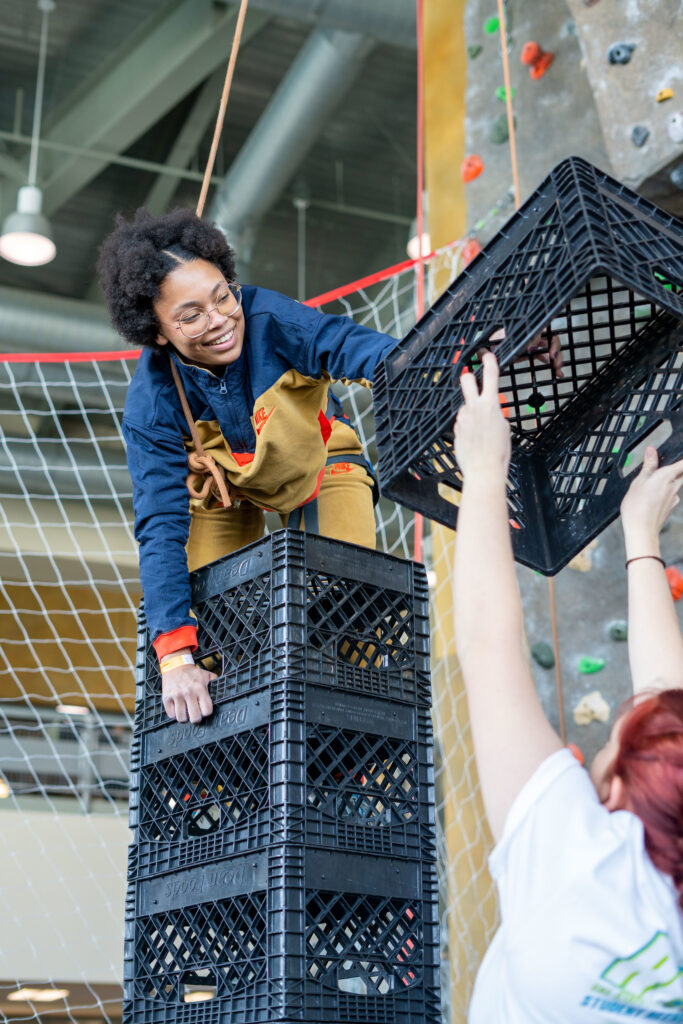 Person on top of a stack of crates being handed another crate.