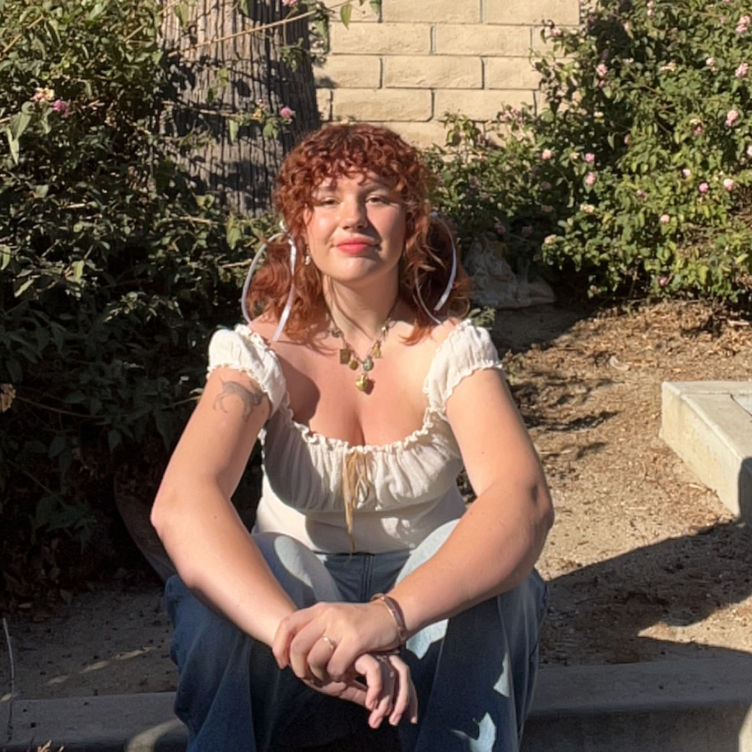 a woman with orange hair sitting on a sidewalk