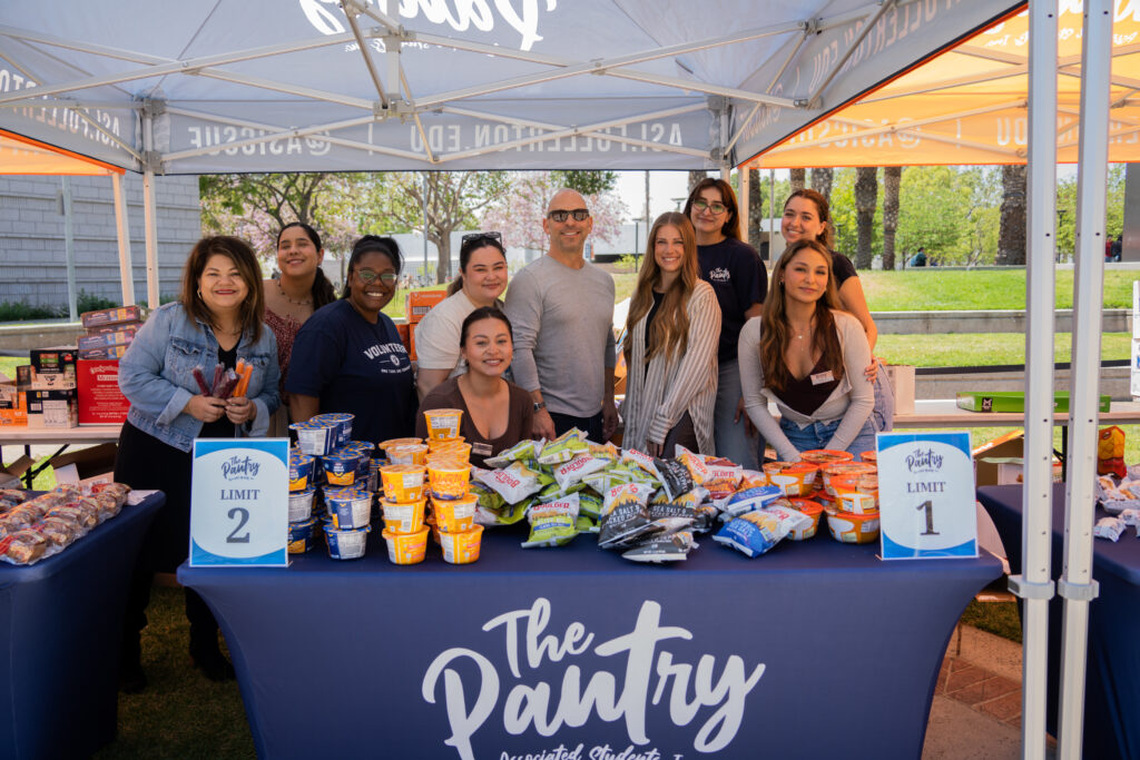 10 people stand in front of a table of food.