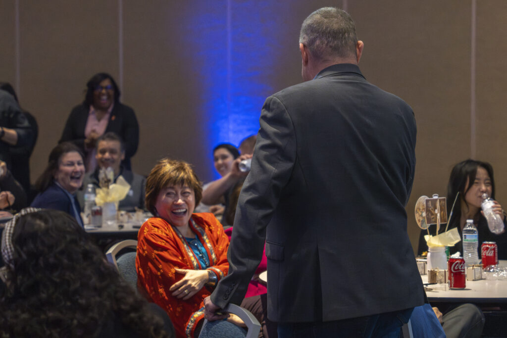 a man talking on a mic as audience smile and laugh