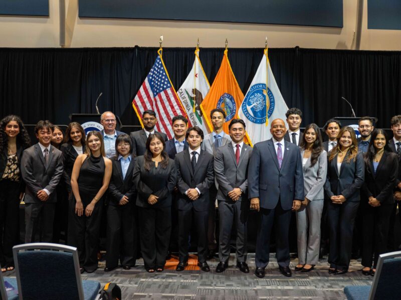 a group of college students in suits stand together for a group picture in front of flags