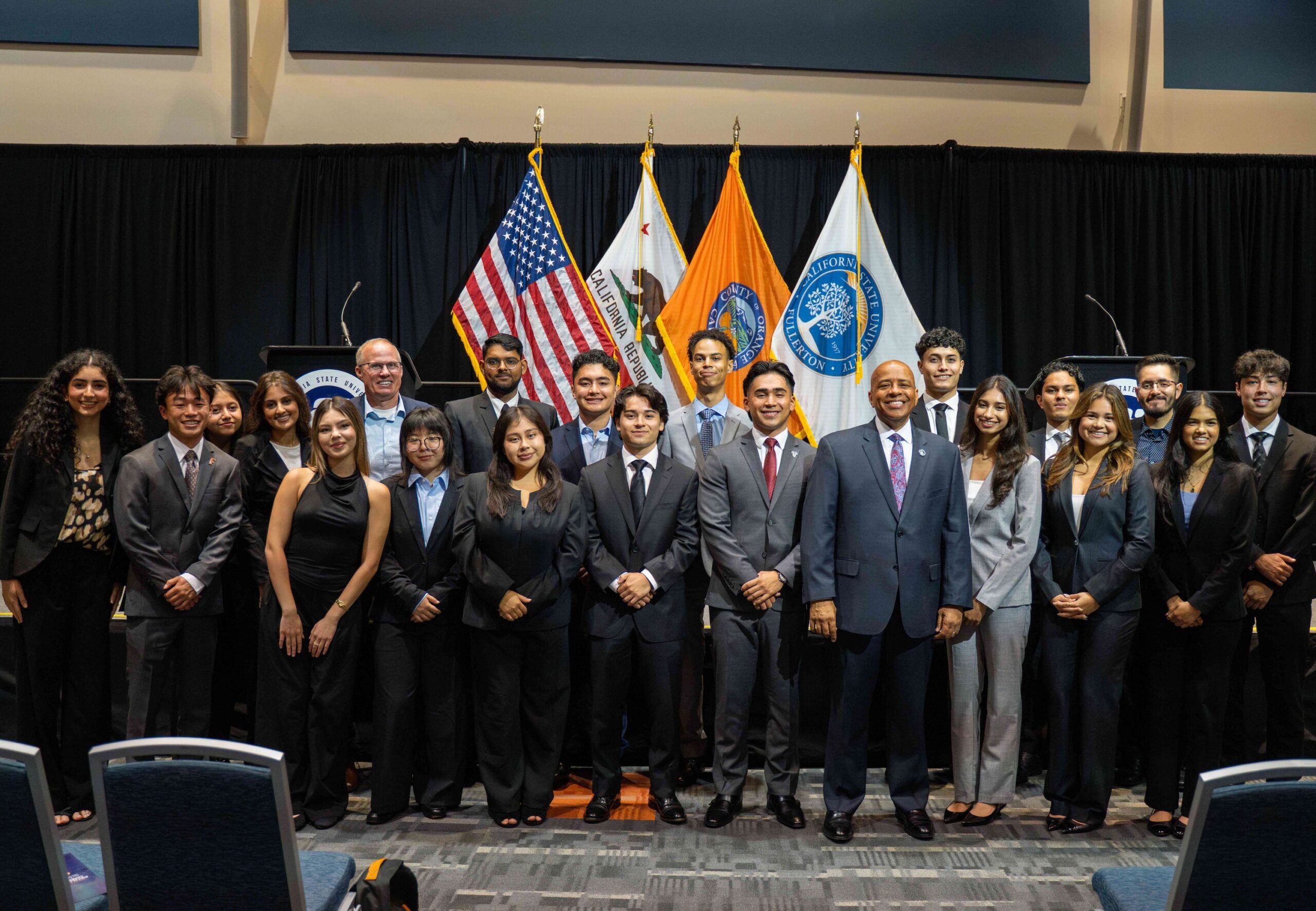 a group of college students in suits stand together for a group picture in front of flags