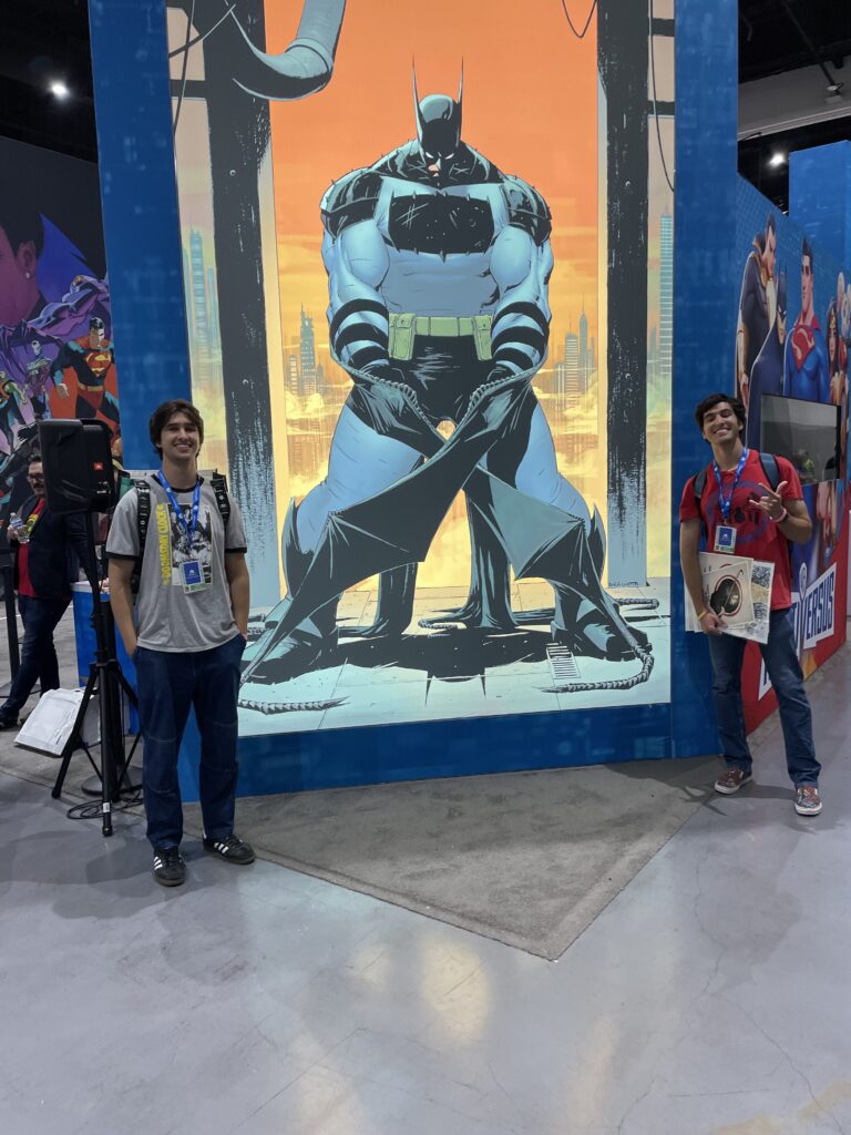 two men standing alongside a tall comic book promotional poster