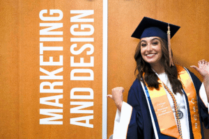 Woman in a graduation cap and gown posed next to a door that says "Marketing and Design."