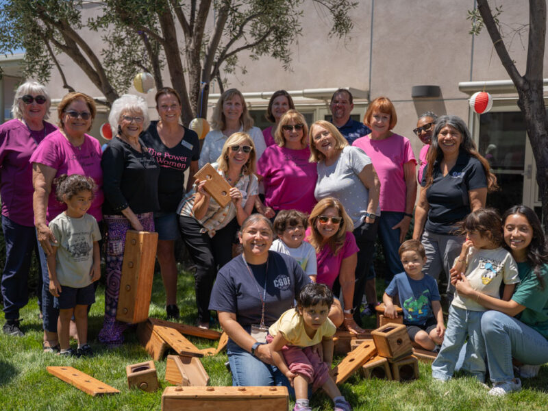 Women and children pose for a group picture holding wooden blocks