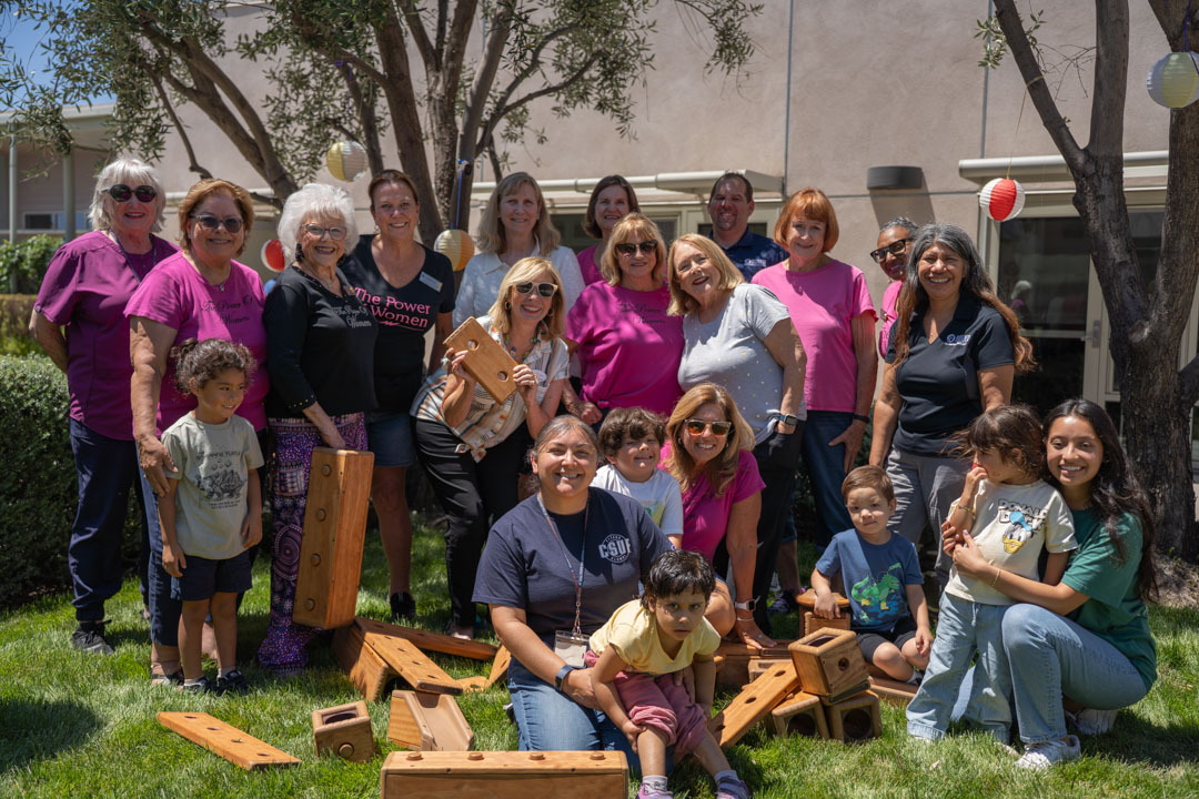 Women and children pose for a group picture holding wooden blocks