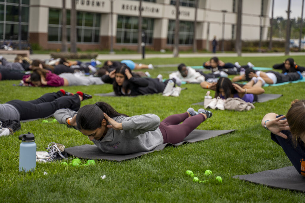 a group of students stretches on the grass during a pilates session