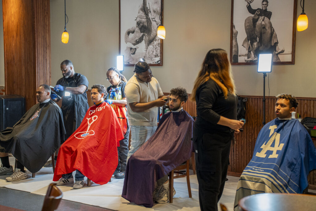 a group of young men getting a haircut in a barbershop setting 
