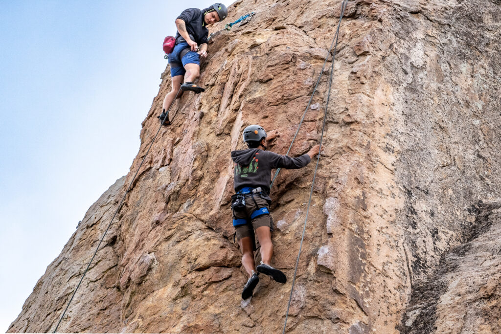 two young men rock climb outdoors