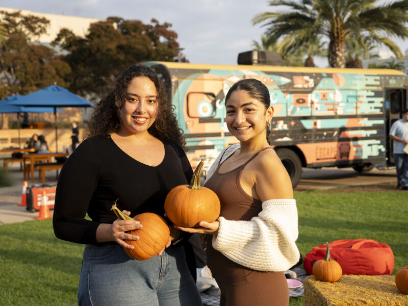 two young women pose for a photo holding pumpkins