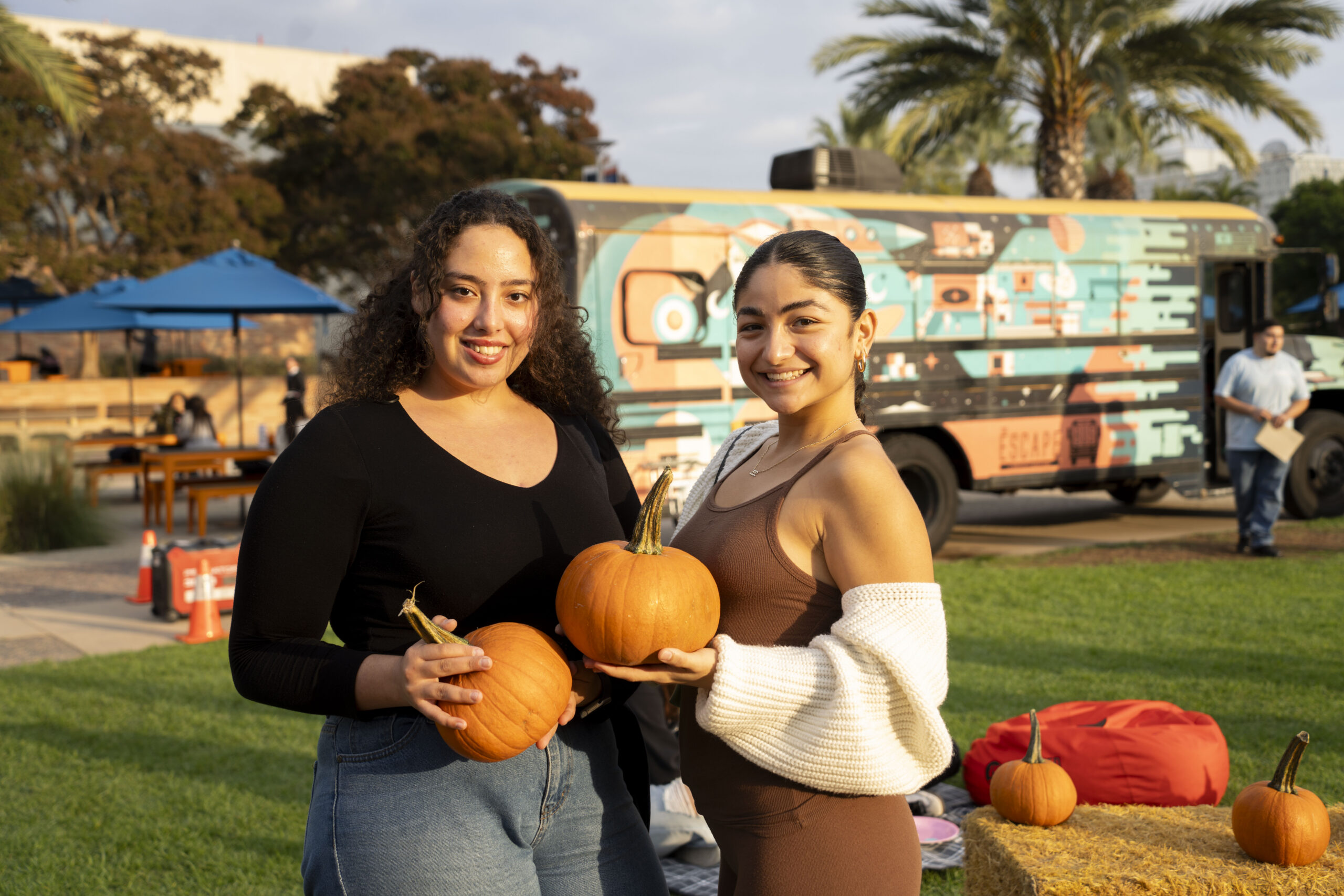two young women pose for a photo holding pumpkins