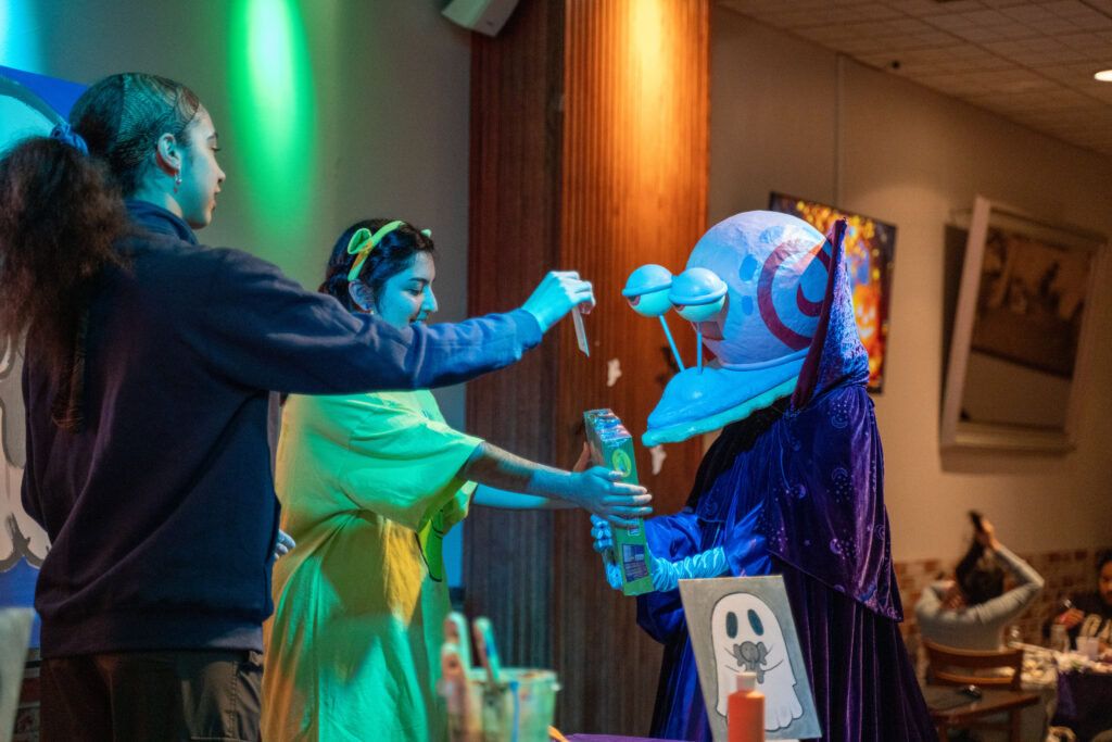 Two people handing student in Halloween costume their prize for winning the costume contest.