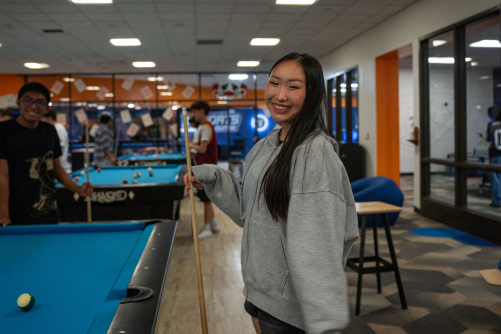 A girl smiles while playing pool. 