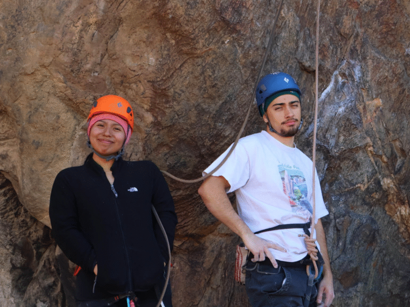 two young climbers pose in front of a rock wall