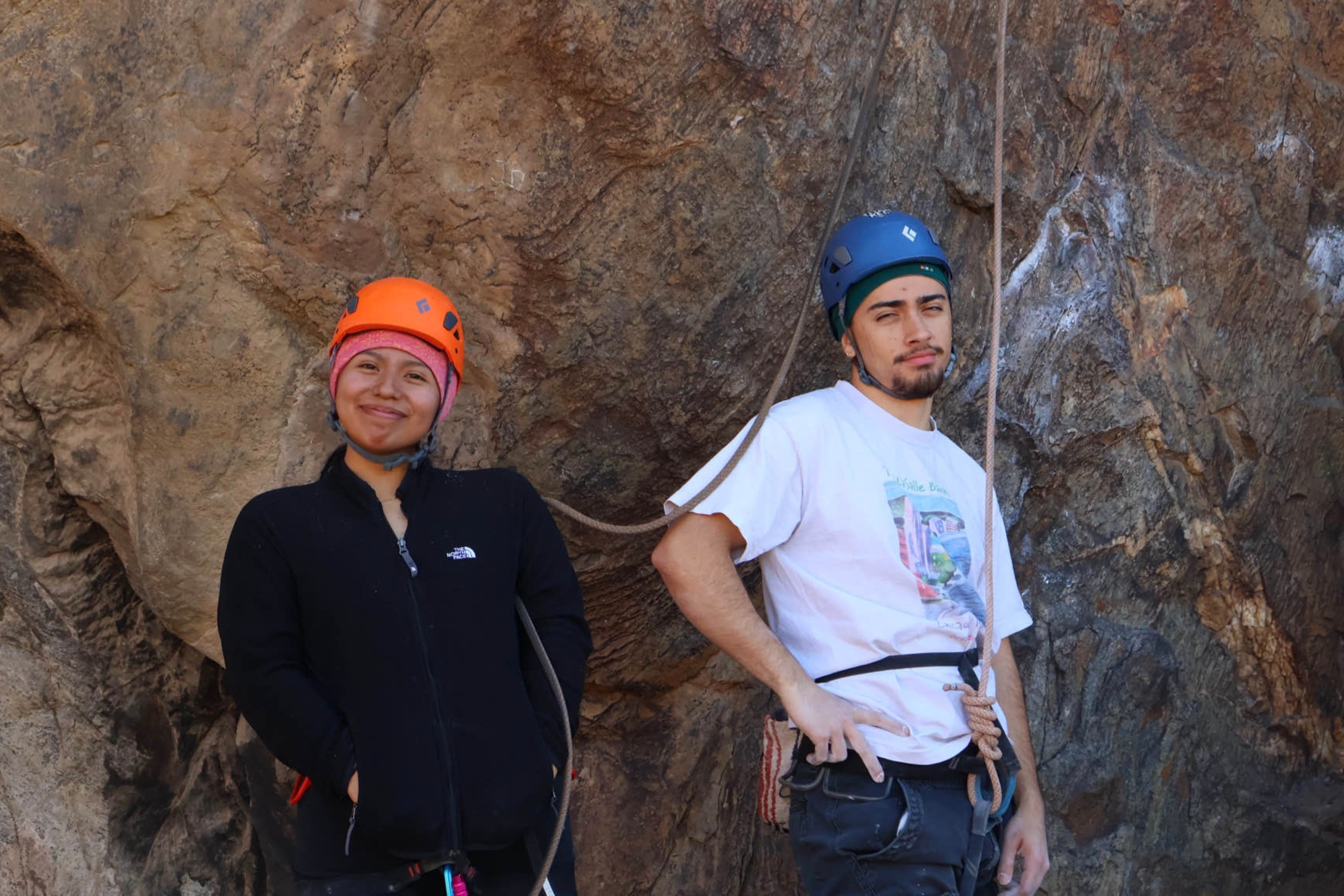 two young climbers pose in front of a rock wall