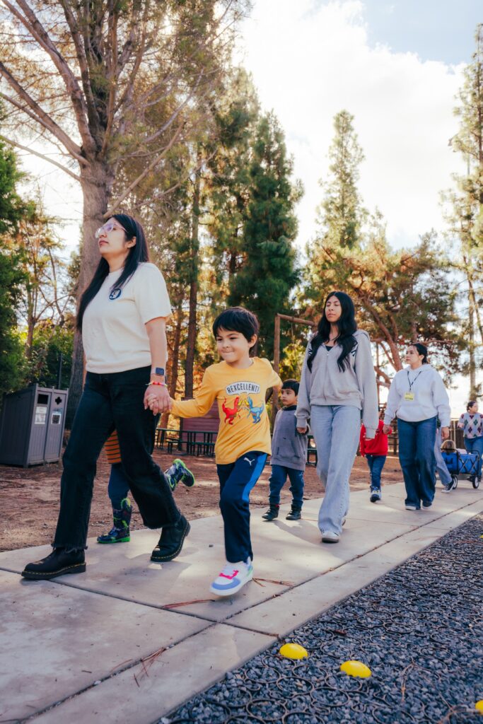 a group of children and adults walk on the sidewalk