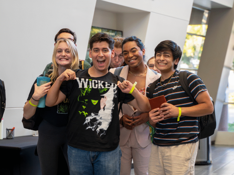 a group of college student Wicked fans pose for a photo showing off their Wicked shirts
