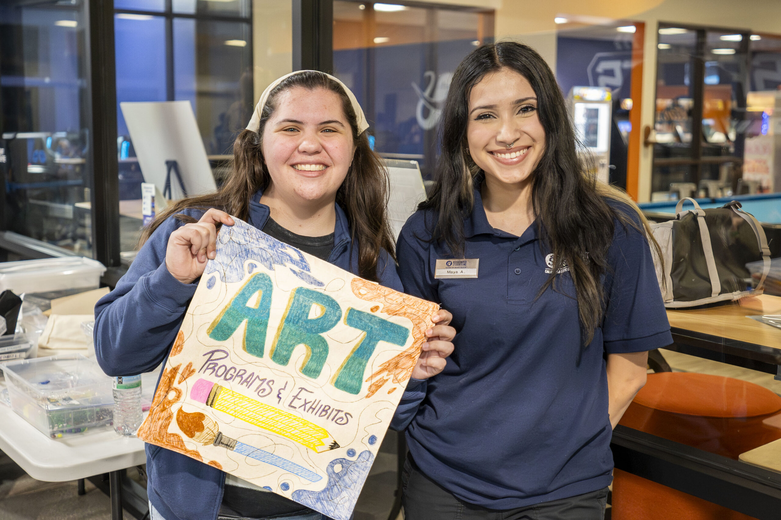 two young women stand together holding up a decorated tote bag