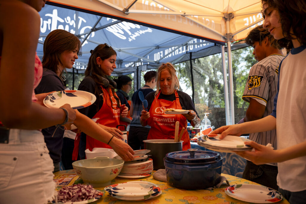 a group of students with orange aprons wait around a table for food.