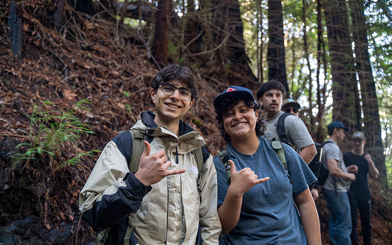 student employees hiking outdoors, giving hang-ten sign