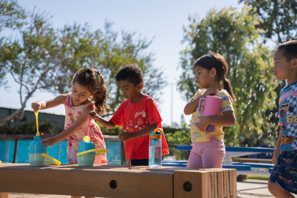 three kids play in a sandbox with bubbles