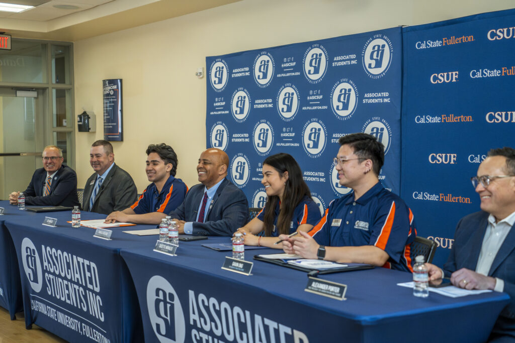 a group of students with staff at a press conference table 