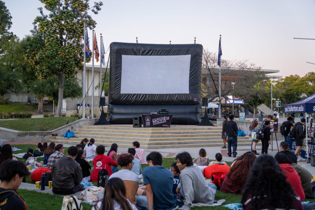 a giant movie screen outdoors with people sitting on grass 
