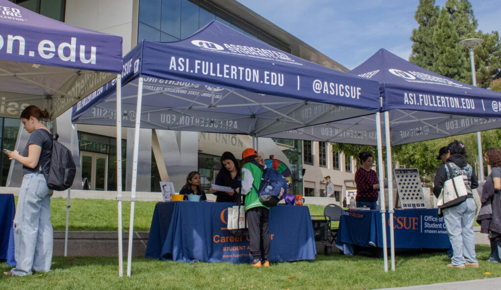 A person in a green jacket and Fullerton logo backpack speaks to two people behind a Career Center table.