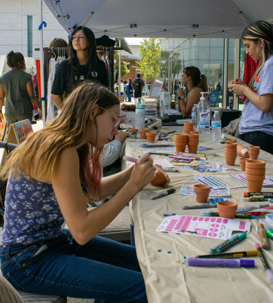 A girl draws on a small clay pot with a marker