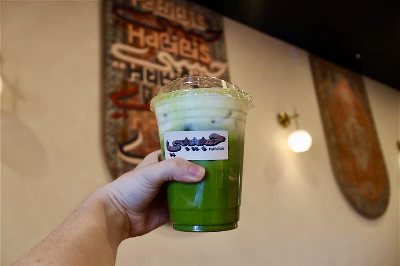 An arm holding a matcha latte inside Habibi's. 