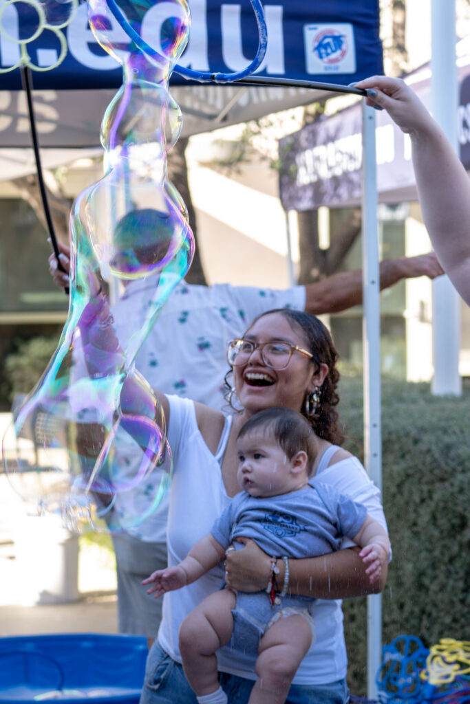 a woman smiles while holding a baby and playing with bubbles