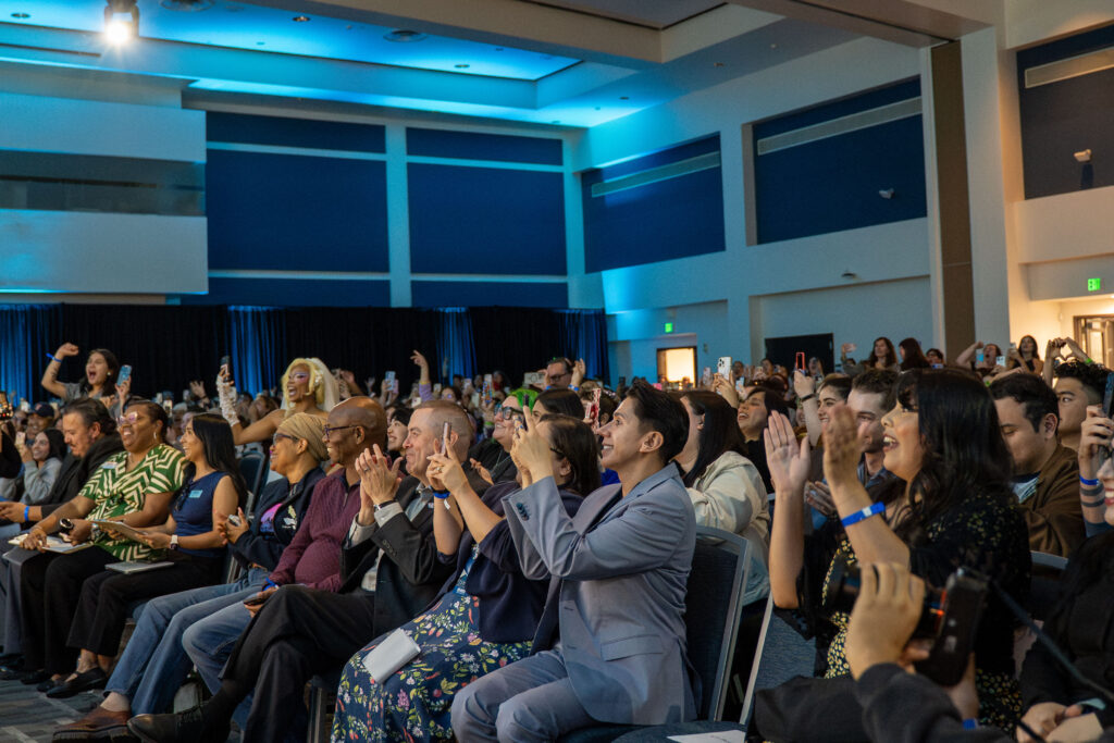 an audience of people with their phones taking pictures and smiling