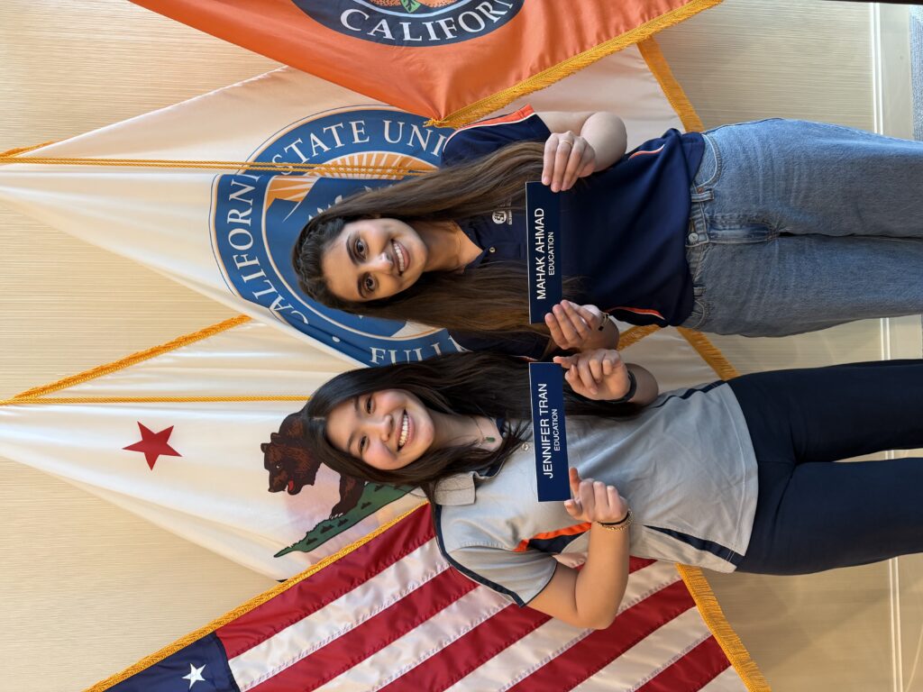 two young women standing in front of the american, orange county and California flag 