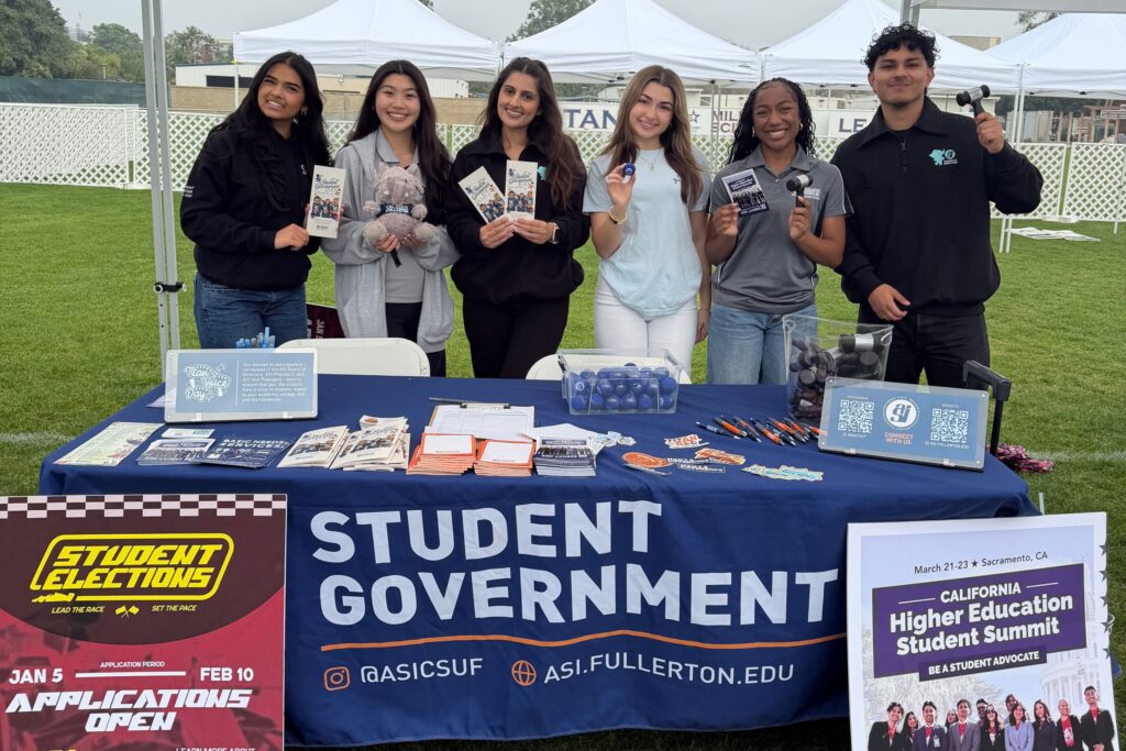 a group of young college students hold up promotional items and flyers under a canopy 