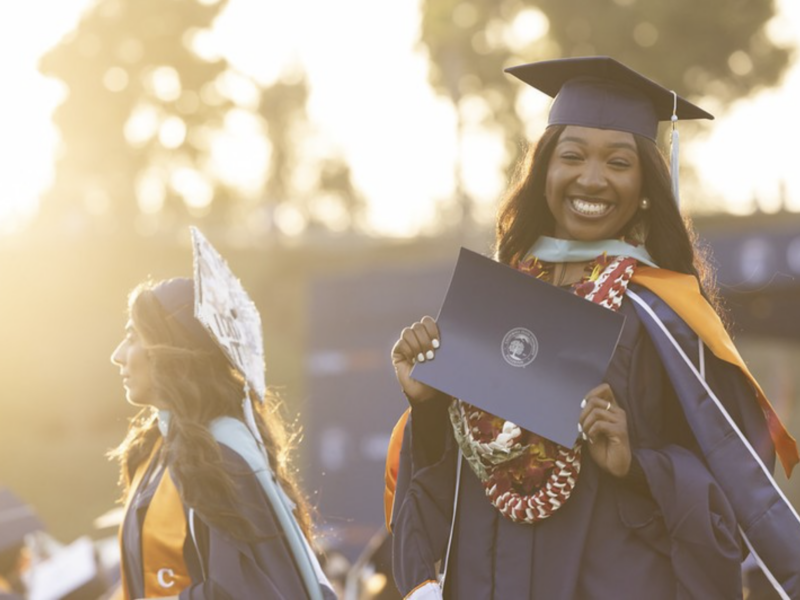 a graduating college student smiles for a photo in regalia